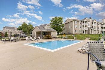 A large swimming pool surrounded by lounge chairs and apartment buildings in the background.